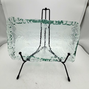 May include: A rectangular clear glass tray with a textured, uneven rim, displayed on a black metal wire stand. The glass features a rippled, organic surface texture throughout the base and edges, providing a translucent appearance.