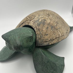 May include: A detailed sculpture of a turtle with a textured, tan-colored shell and green body. The turtle's head is extended, and its flippers are spread out. The sculpture is made of a material that appears to be stone or ceramic.