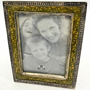 May include: A rectangular photo frame with a metallic, beaded outer border and an inner border featuring a yellow and green swirling pattern. The frame holds a black and white photograph with text reading 2.5" X 3.5" and MYX.
