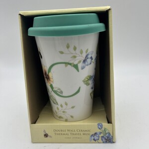 May include: White double-wall ceramic travel mug with a green lid, floral and bee design, and the letter "C". The mug is in a cardboard box with text that reads "DOUBLE WALL CERAMIC THERMAL TRAVEL MUG 12oz (355ml)".