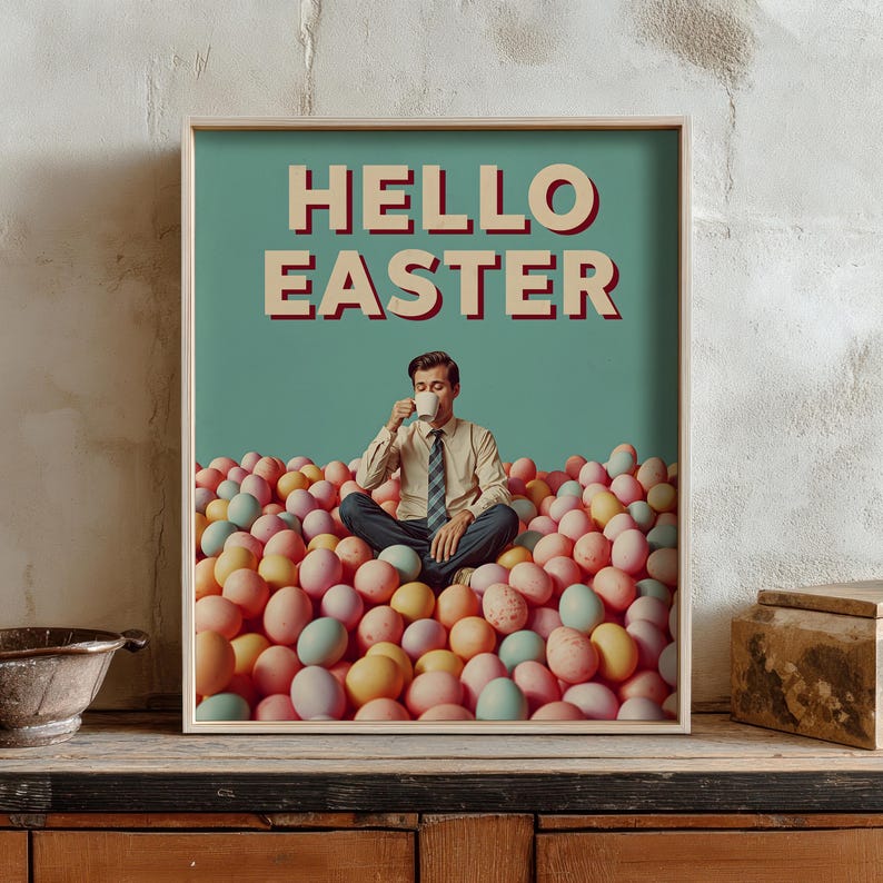 May include: A framed print featuring the text "HELLO EASTER" above a man seated amongst pastel Easter eggs, drinking from a mug. The background is a teal colour, with a wooden frame.