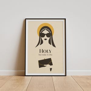 Puede incluir: Impresión artística enmarcada con una ilustración estilizada de una mujer con gafas de sol y un halo, sosteniendo un bolso de mano negro. El texto "HOLY but make it chic" está en una fuente moderna. Fondo crema.