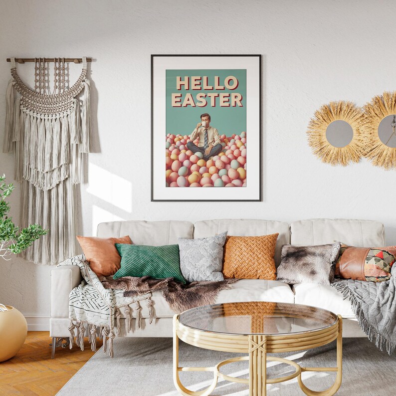 May include: A framed poster with the text "HELLO EASTER" above an image of a person sitting in a pile of Easter eggs. The room features a white sofa with colourful cushions, a round coffee table, and decorative wall hangings.