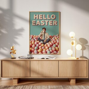 May include: A framed poster with the text "HELLO EASTER". The image features a person in a pile of Easter eggs, drinking from a cup. The poster is above a wooden cabinet. The cabinet has a modern design.