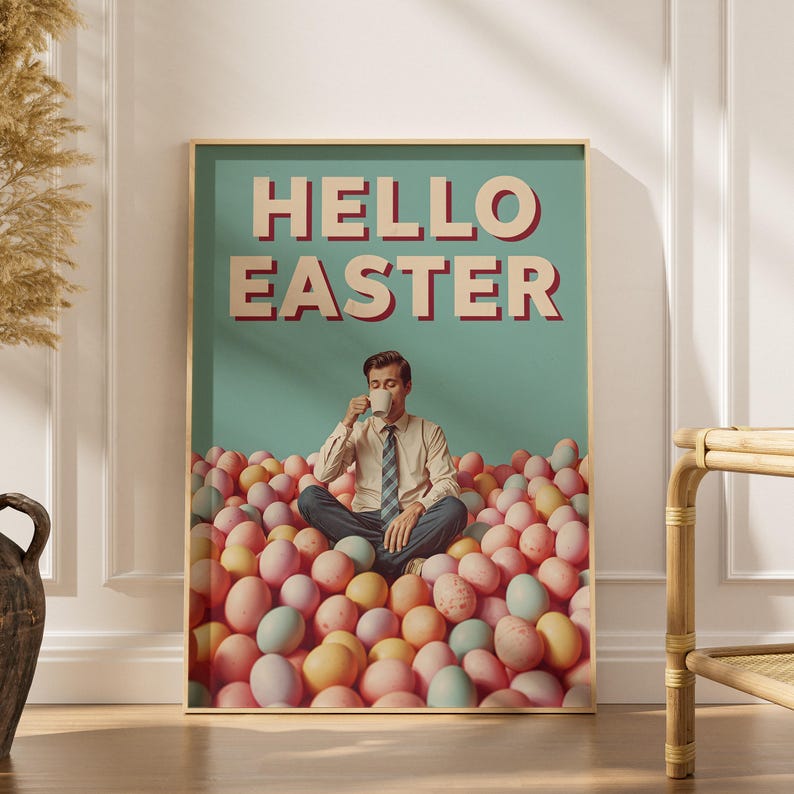 May include: A framed poster with the words "HELLO EASTER" in red and white. The poster shows a person sitting in a pile of pastel-coloured Easter eggs, drinking from a mug. The background is a light teal colour.