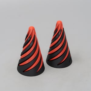 May include: Two black and red cone-shaped objects. The cones have a spiral design with alternating black and red sections. The objects are standing upright against a plain, light background.