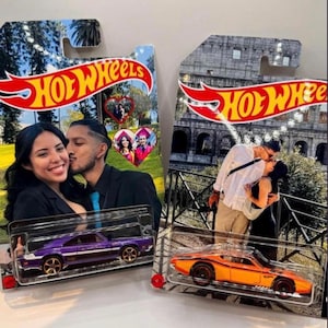 Op de afbeelding: Twee Hot Wheels speelgoedauto's in verpakking. Eén is paars met gouden wielen, de andere is oranje met zwarte strepen. De verpakking bevat foto's van stellen en het Hot Wheels logo.