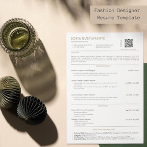 Puede incluir: Una plantilla de currículum vitae para un diseñador de moda, con el texto "Fashion Designer Resume Template" en la parte superior. El currículum incluye secciones para resumen, experiencia laboral, educación e información adicional. Un vaso decorativo y dos adornos de papel están en la imagen.