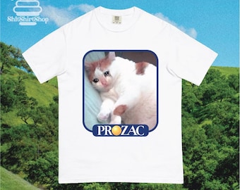 May include: White t-shirt featuring a meme of a sad cat with the word "PROZAC" below the image. The shirt has a crew neck and short sleeves. The brand logo "ShitShirtShop" is visible in the upper left corner.