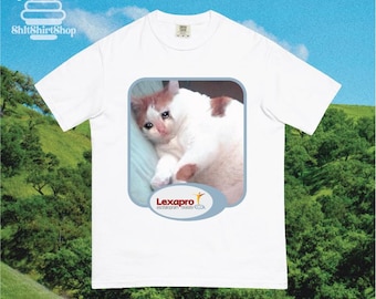 May include: White t-shirt featuring a meme of a sad cat with brown and white fur. The cat image is inside a blue rounded rectangle with the word "Lexapro" and a logo. The shirt has the text "ShitShirtShop" at the top.