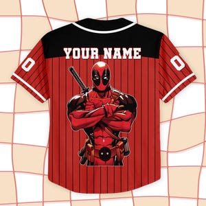 K&ouml;nnte beinhalten: Rotes und schwarzes Baseball-Trikot mit dem Text "YOUR NAME" auf dem R&uuml;cken. Das Trikot zeigt eine Deadpool-Grafik auf dem R&uuml;cken und die Nummer "0" auf den &Auml;rmeln. Das Trikot hat einen schwarzen Kragen und wei&szlig;e Verzierungen.