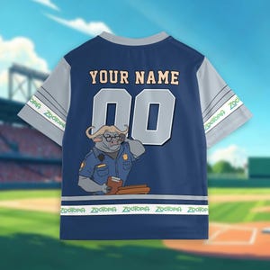 May include: Navy blue baseball jersey with gray sleeves. The back features the text "YOUR NAME" above the number "00" in gray. A cartoon buffalo police officer is on the back. The bottom has the text "Zootopia" in green and white.