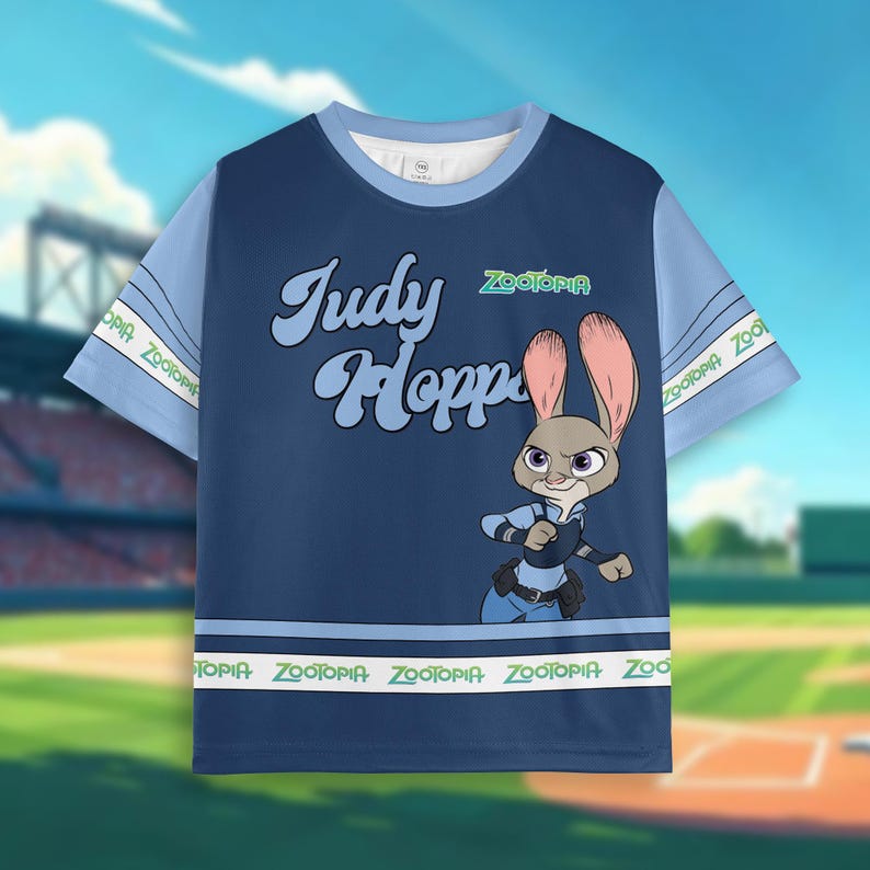 Puede incluir: Camiseta azul marino con Judy Hopps de Zootopia. La camiseta tiene mangas y ribetes azul claro con la palabra "Zootopia" impresa. El dise&ntilde;o incluye el texto "Judy Hopps" en una fuente retro.
