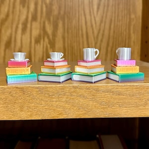May include: Four miniature stacks of books, each topped with a teacup and saucer. The books are in various colors, including green, orange, pink, and yellow. The teacups and saucers are white.