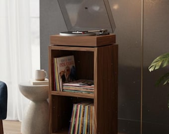 Puede incluir: Un mueble de tocadiscos de madera con un tocadiscos en la parte superior y dos estantes llenos de discos de vinilo. Una lámpara de pie dorada y una planta en maceta están junto al mueble. Un sillón azul y una mesita auxiliar pequeña están en el fondo.