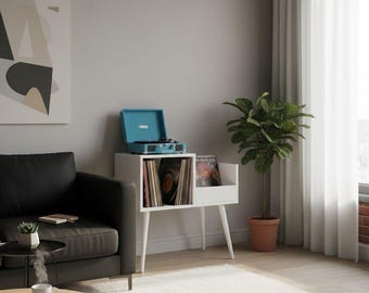 May include: A white mid-century modern record player stand with a turquoise record player on top. The stand has a compartment for vinyl records and a small shelf. A potted plant and a black sofa are also in the room.