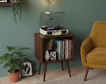 May include: A mid-century modern record player on a dark wood cabinet with a shelf of vinyl records. The cabinet has angled legs and is next to a yellow armchair and a potted plant. A wall-mounted light fixture is above the cabinet.