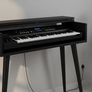 May include: A black digital piano with white and black keys, set in a black wooden stand with angled legs. The piano has a display screen and various control buttons. The stand has a built-in shelf and a top cover.