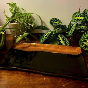 May include: A rectangular serving tray featuring a glossy black finish on the main surface and a textured, metallic copper-colored band along one edge. The tray has slightly wavy, uneven edges and a smooth, reflective center section.