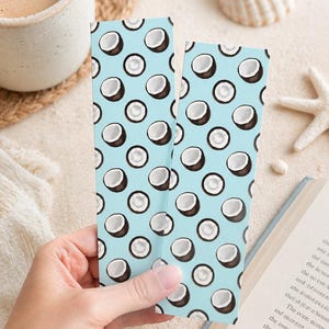 May include: Two rectangular bookmarks featuring a repeating pattern of halved brown coconuts with white centres against a light blue background. The bookmarks are narrow and vertical, displaying a consistent graphic design of tropical fruit.