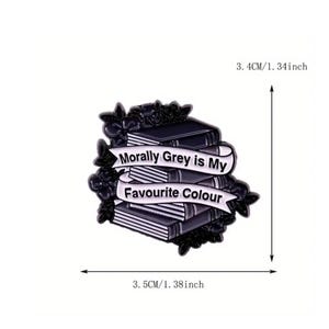 May include: A black and white enamel pin featuring a stack of books surrounded by floral details. A white banner across the books reads "Morally Grey is My Favourite Colour". The pin measures 3.4 inches by 3.5 inches as indicated by the arrows.