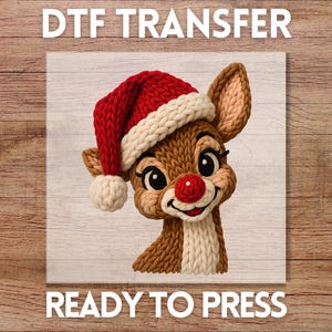 May include: A DTF transfer featuring a cartoon reindeer wearing a red and white knit Santa hat and a red nose. The reindeer is made of brown and cream-colored knit material. The text "DTF TRANSFER" and "READY TO PRESS" are displayed in white.