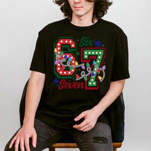 A person wearing a black t-shirt with a colorful design featuring the number '67' and the text 'Seventh' on it.