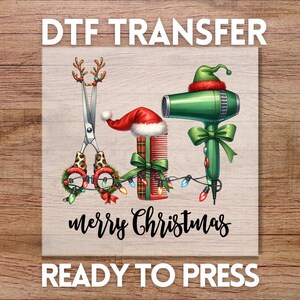 May include: A Christmas-themed DTF transfer design featuring salon tools: scissors with reindeer antlers, a comb, and a hair dryer, all adorned with Santa hats and festive lights. The words "merry Christmas" and "ready to press" are also included.
