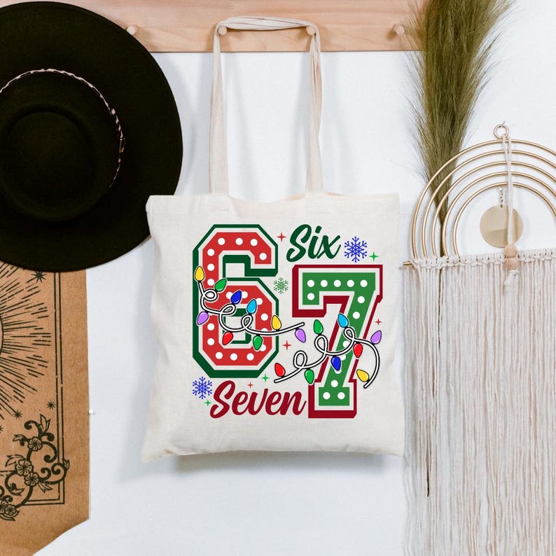 A white tote bag with the number "67" printed on it, surrounded by colorful lights and snowflakes, hanging on a wall.