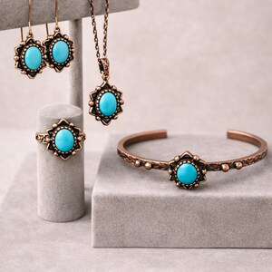 Könnte beinhalten: Ein Schmuckset mit einem türkisfarbenen Stein in einer bronzefarbenen Fassung. Das Set umfasst Ohrringe, eine Halskette, einen Ring und ein Armband. Die Ohrringe sind im Tropfenstil gehalten, und das Armband ist ein Armreif.