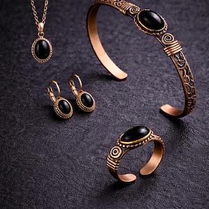 May include: A jewellery set comprising a necklace, earrings, bracelet, and ring. Each item has a gold-coloured metal setting with an oval black stone. The bracelet and ring have decorative details. The jewellery is displayed on a dark surface.