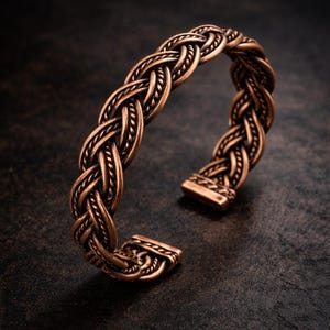 May include: A bronze-colored cuff bracelet with a braided design. The open cuff features a detailed woven pattern, showcasing a blend of texture and craftsmanship. The bracelet is displayed against a dark background.