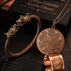Puede incluir: Un conjunto de joyería en tono cobre que incluye un brazalete trenzado con dos cabezas de lobo, un collar con colgante circular con símbolos grabados y caligrafía árabe, y un anillo abierto con un diseño de estrella geométrica.