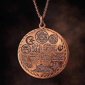 May include: A gold-colored pendant necklace with a detailed circular charm. The charm features intricate engravings of symbols and text, including a star and crescent, and other religious iconography. The pendant hangs from a delicate chain.
