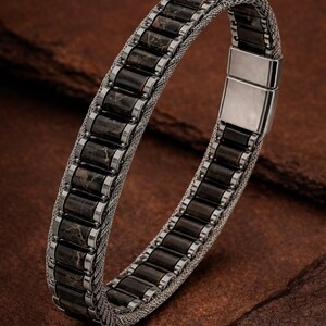 May include: A bracelet featuring a series of rectangular dark brown stone segments with light brown veining, set within a silver-toned metal frame. The band consists of a woven silver-toned mesh chain and includes a smooth, rectangular metal clasp closure.