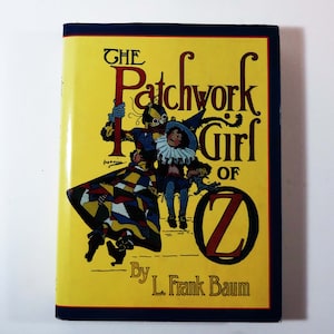 May include: A yellow book cover with the title "The Patchwork Girl of Oz" by L. Frank Baum. The cover features an illustration of a patchwork girl and a man with a patchwork suit.