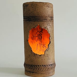 May include: A brown ceramic lamp with a cutout revealing a glowing orange light and a carved image of a person holding a bow and arrow.