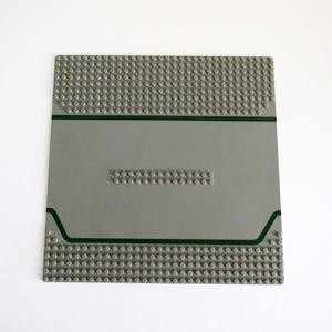 May include: A gray Lego baseplate with a green border and a row of studs in the center.
