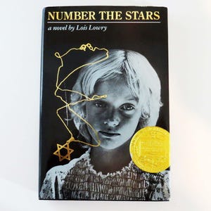 May include: A black and white cover of the book "Number the Stars" by Lois Lowry. The cover features a young girl with blonde hair and a gold Star of David necklace. The book has won the Newbery Medal.