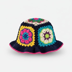 May include: A navy blue crochet bucket hat with a colorful floral pattern. The hat features a square design with bright pink, yellow, teal, and green accents. The brim is trimmed with a bright pink border.