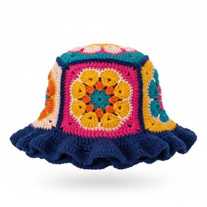 May include: A colorful crochet bucket hat with a square crown and a ruffled brim. The hat features a vibrant patchwork design with pink, yellow, orange, and teal squares, and a dark blue ruffled edge. The hat is a stylish accessory.