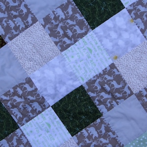 May include: A patchwork quilt with a variety of patterns, including animals, leaves, and text. The quilt is made in shades of brown, green, white, and light blue.