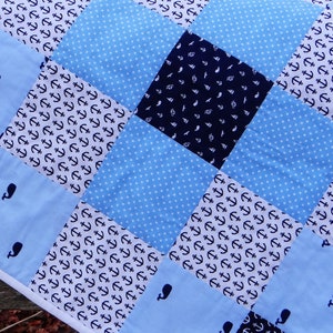 May include: A blue and white baby quilt with a patchwork design featuring anchors and whales. The quilt is made of different fabrics with various patterns.