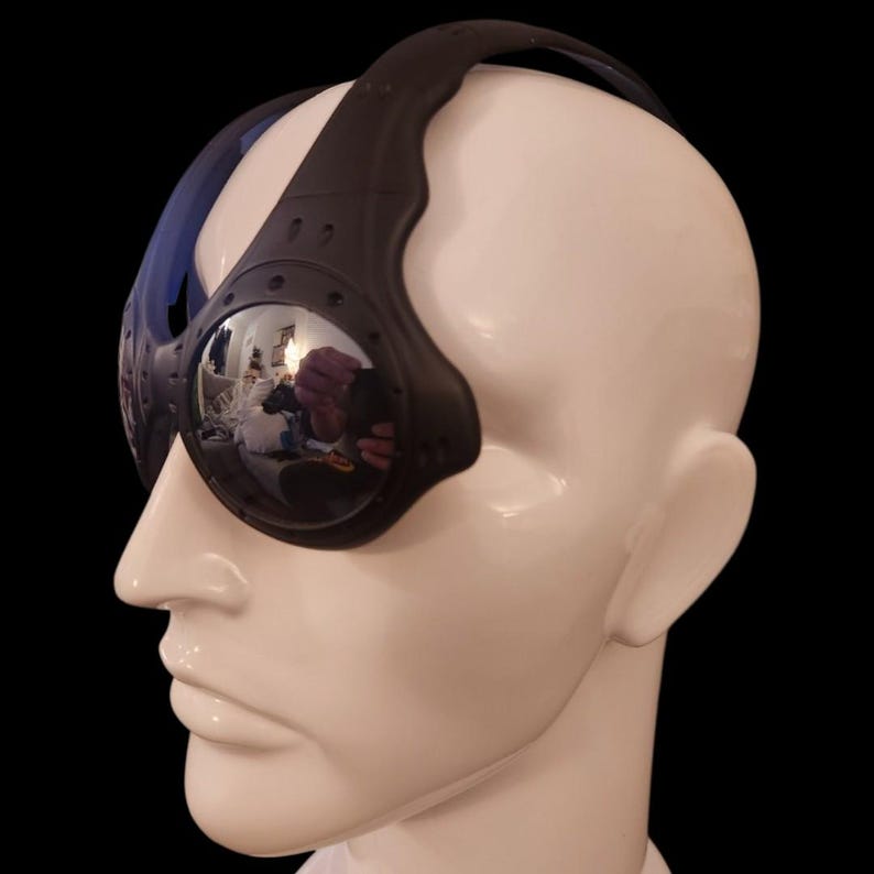 May include: Black and blue sports goggles with mirrored lenses. The goggles have a thick black frame and a blue strap. The lenses reflect the surrounding environment. The goggles are displayed on a white mannequin head against a black background.