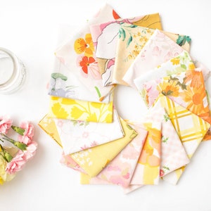 May include: A collection of vintage floral fabric squares arranged in a circular pattern. The fabrics feature various floral patterns in shades of yellow, pink, and orange. A small glass jar and a bouquet of yellow and pink flowers are also present.