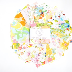 Puede incluir: Un conjunto de cuadrados de tela coloridos con estampados florales en tonos amarillos, naranjas, rosas y azules. Los cuadrados están dispuestos en un patrón circular alrededor de una tarjeta que dice "Vintage Sheet 15 Charm Pack 5" x 5" Charm Squares."