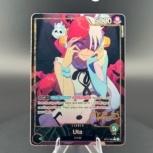 May include: A collectible trading card featuring a character with red and white hair, a blue and white outfit, and the text "Uta." The card has a gold foil signature and the text "Gold Foil Signature" at the top. The card is displayed on a clear stand.
