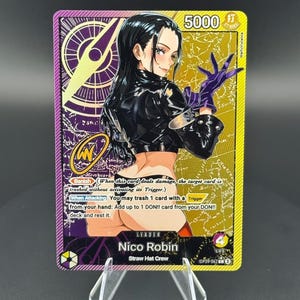 May include: A One Piece trading card featuring Nico Robin as a leader. The card has a purple and gold background with a map design, a power level of 5000, and text including Banish, When Attacking, and Straw Hat Crew. The character wears a black jacket.