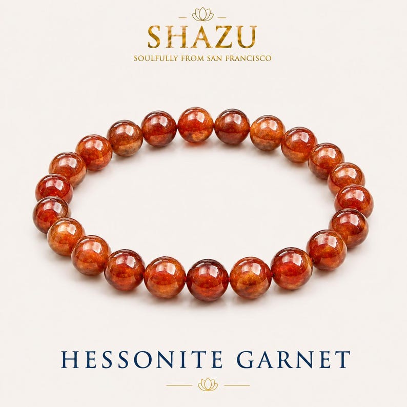 Pode incluir: Uma pulseira circular composta por contas de granada hessonita redondas, polidas e transl&uacute;cidas de cor laranja acastanhada. O texto SHAZU SOULFULLY FROM SAN FRANCISCO aparece no topo e HESSONITE GARNET est&aacute; impresso na base.