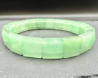 Può includere: Un braccialetto verde chiaro composto da perline rettangolari traslucide. Il braccialetto è fatto di una pietra verde chiaro ed è esposto su una superficie grigia. Il braccialetto è un gioiello.